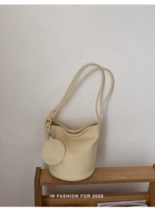 Detail of cream leather bucket bag with matching round coin purse charm on a wooden shelf