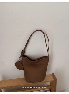 Close-up of a brown retro bucket bag with long strap and round leather pendant detail