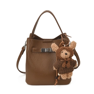 Brown lychee texture bucket bag with top handle and plush bear charm on white background