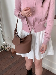Brown minimalist leather bucket bag with shoulder strap and round charm on female model