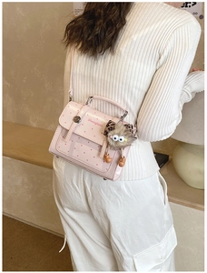 Pink polka dot handbag with plush charm shown worn by a model in a minimal interior