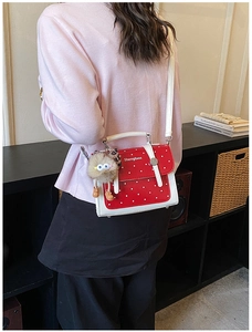 Detailed shot of red polka dot handbag with cute plush monster pendant and white strap