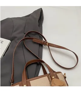 Détail de la bandoulière réglable en cuir marron et chaîne dorée sur le sac seau contrasté