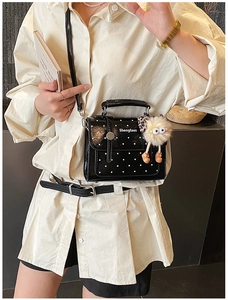 Chic black polka dot handbag with glossy finish and cute plush charm on a model