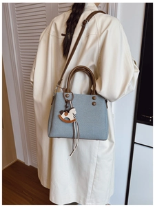 Detail of light blue woven handbag featuring leather handles and a rocking horse charm