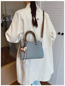 Detail of light blue handbag with brown handles, fabric texture, and cute horse charm