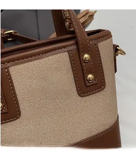 Détail d'un sac à main en tissu tissé beige avec garniture en cuir brun et rivets dorés
