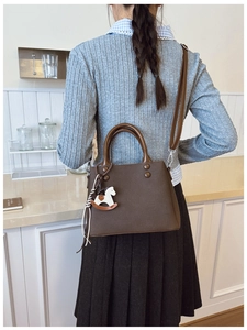 Brown leather trapezoid bag detail with white rocking horse charm and rivet accents