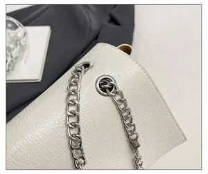 Gros plan du sac chaîne blanc crème montrant le cuir froissé brillant et le métal argenté