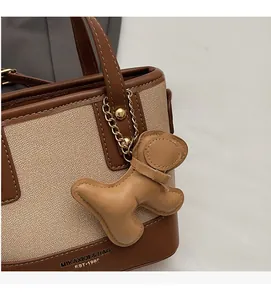 Détail du sac seau en toile avec garniture en cuir brun et charm de chiot sur la poignée