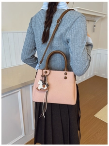 Pink crossbody bag detail showing contrast brown handles and a wooden horse charm