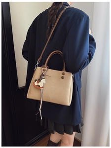 Detail of a large beige tote bag with brown handles and a leather horse charm on shoulder