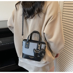 Détail du mini sac bandoulière bicolore avec bordure en cuir et accessoire de charme chiot