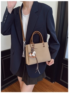 Detail view of khaki canvas crossbody bag with leather handles and rocking horse charm