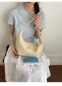 Detail showing creamy beige hobo shoulder bag with litchi grain texture worn by model