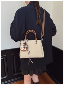 Detail of beige canvas tote bag featuring brown leather straps and wooden pony charm