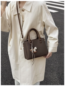 Detail of deep brown crossbody bag with horse charm on a model in beige coat