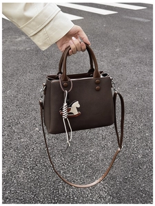 Detail of dark brown leather handbag with horse charm on a city street background
