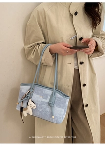 Détail du sac cabas bleu clair à texture carrée et pendentif cheval sur un trench beige