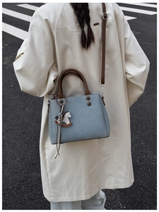 Detail of grey-blue handbag with leather handle and decorative rocking horse charm