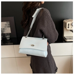Détail d'un sac bandoulière bleu clair avec fermoir rotatif argenté et chaîne métallique