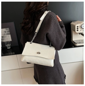 Détail d'un sac baguette en cuir crème avec bandoulière chaîne argentée sur un modèle