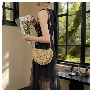 Close-up of crescent straw bag with lace wave edges and brown leather strap on model