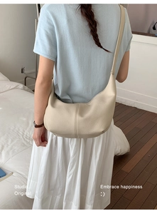 Detailed view of beige pleated crescent bag with pebbled leather texture and stitching