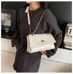 Détail du sac bandoulière en cuir crème avec chaîne argentée et fermoir rotatif en métal