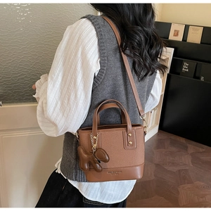 Close-up of caramel bucket bag with litchi texture and a cute dark brown puppy charm