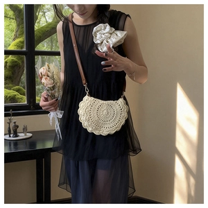 Detail of a beige woven crossbody bag with scalloped edges and a brown shoulder strap
