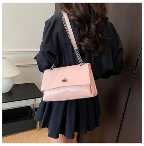 Sac sous le bras rose à chaîne porté par un modèle sur fond sombre de maison