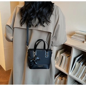 Detail of black bucket bag with a small dog charm against a minimalist shelf