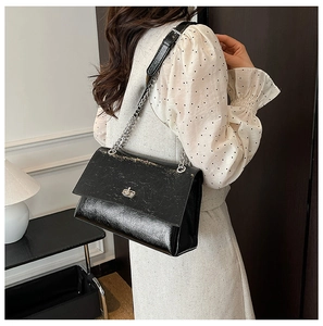 Détail du sac bandoulière en cuir froissé noir avec chaîne argentée et fermoir pivotant