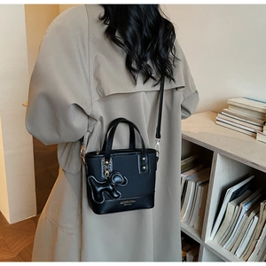 Détail d'un sac seau noir avec garniture dorée et breloque chien porté par mannequin