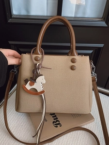Khaki fabric tote bag with brown leather handles and a horse charm on a book