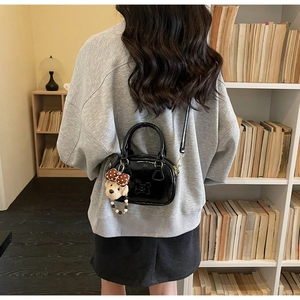 Vue détaillée d'un sac bandoulière en cuir verni noir avec un ours en peluche mignon