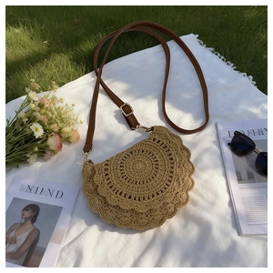 Straw saddle bag with woven wave pattern and leather strap on a summer picnic mat