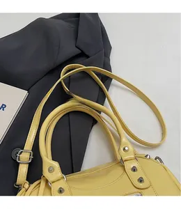 Detailed close-up of yellow leather Boston bag with metallic rivets and shoulder strap