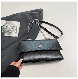 Détail du sac noir brillant avec fermoir rotatif argenté et bandoulière chaîne