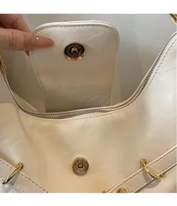 Dettaglio della fibbia magnetica dorata su borsa in pelle color crema con incisioni