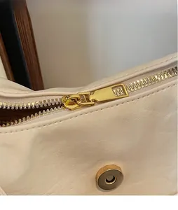 Dettaglio macro della cerniera dorata liscia e della chiusura magnetica sulla borsa beige