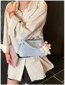 Close-up of light blue suede shoulder bag with metal logo and cute bear plush charm