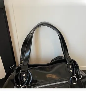 Detail of glossy black faux leather tote with silver zipper and metallic rivets