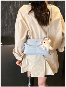 Detail of light blue faux leather crossbody bag with a plush bear charm on a model