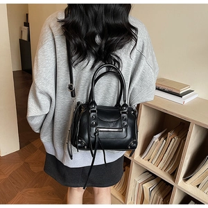 Detail of black riveted Boston bag with long tassels shown on model in a cozy room