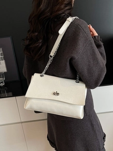 Sac sous le bras blanc crème avec chaîne en argent porté par un mannequin en studio