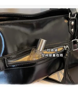 Close-up of black glossy leather tote bag showing external silver zipper pocket detail