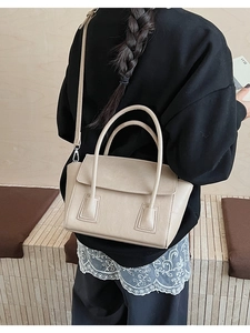 Detail of elegant beige crossbody bag with lychee texture and slim strap over black hoodie