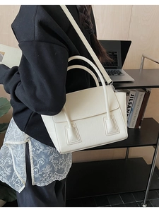 Minimalist cream white leather handbag with dual handles and crossbody strap on desk